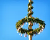 En midsommarstång, dekorerad med grönt och band, mot en klarblå himmel. Dess midsommarstång betydelse symboliserar sommarsolståndet och fruktbarhet.