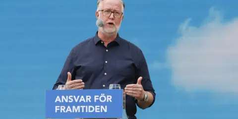 Man med glasögon och mikrofon talar vid ett podium med texten "Ansvar för framtiden". Hans gestik och budskap speglar en liberalism ideologi.