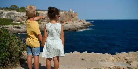 Två barn står vid havet, redo för sommarlåtar och skolavslutning. Pojken pekar mot horisonten.