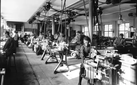 Barn arbetar vid maskiner i en verkstad, en scen från den industriella revolutionen.