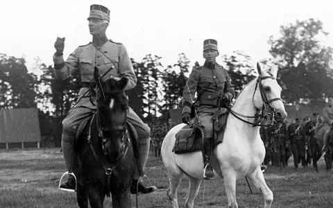 Två militärer till häst, kanske under en övning för regementen i Sverige. Bakom syns fler soldater och träd.