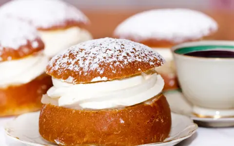 Semlor, en fest vid fastan, pudrade med florsocker och fyllda med grädde. En kopp kaffe i bakgrunden.