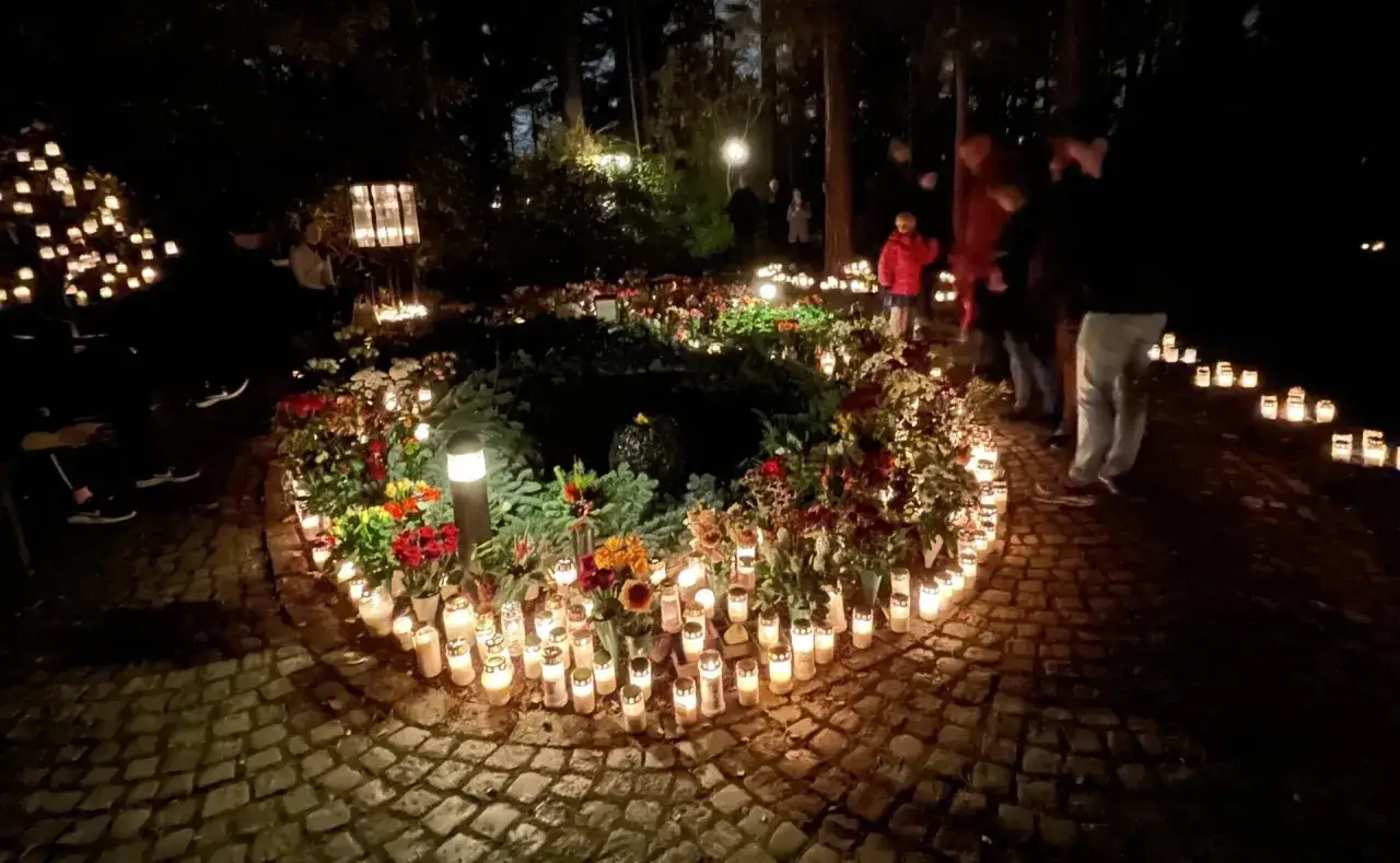 Många ljus lyser upp en gravplats under all helgons dag. Blommor och människor syns i mörkret.