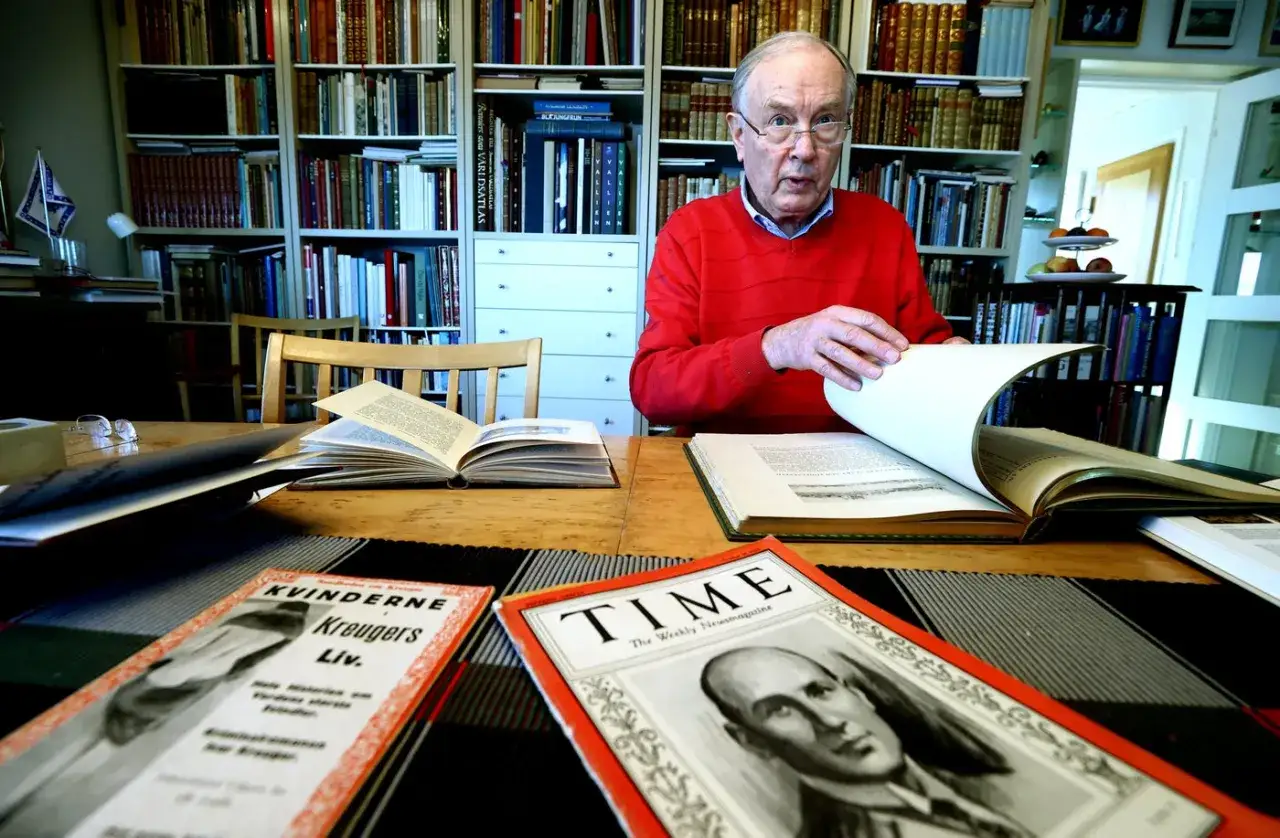 &Auml;ldre man i r&ouml;d tr&ouml;ja bl&auml;ddrar i bok. P&aring; bordet ligger b&ouml;cker och tidningar, bland annat en om Kvinnorna Kreugers liv.