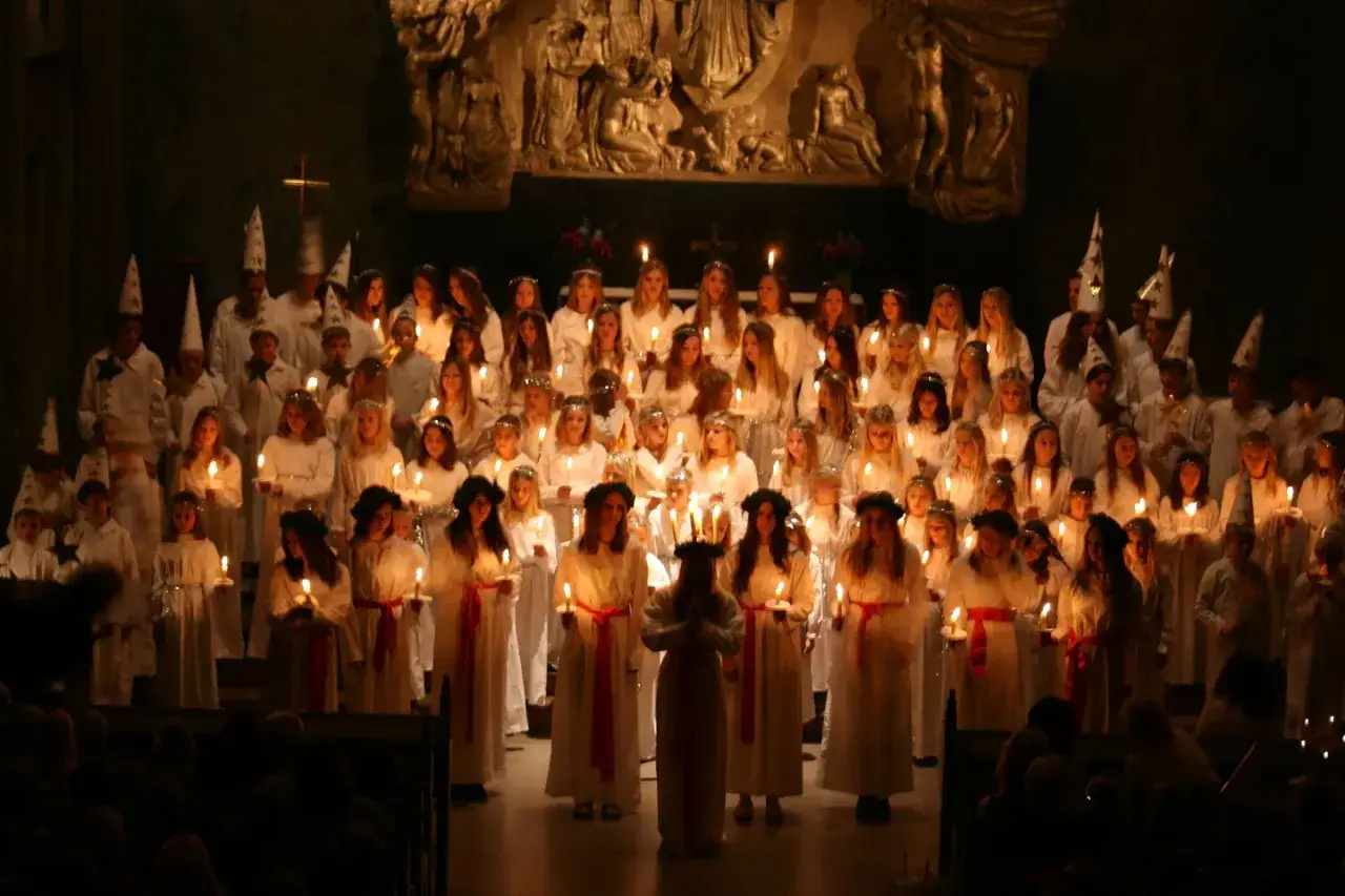 En stor k&ouml;r av barn och ungdomar i vita kl&auml;der och ljusa hattar deltar i en st&auml;mningsfull lucia konsert.