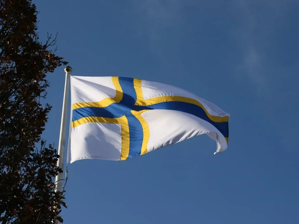 Sverigefinnarnas dag firas med en vit flagga med bl&aring;tt och gult kors som vajar i vinden mot en klarbl&aring; himmel.