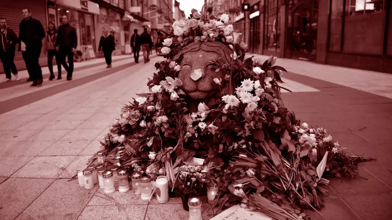 Minnesplats med blommor och ljus efter terrordådet på Drottninggatan. En stenlejon pryds av blomsterkrans.